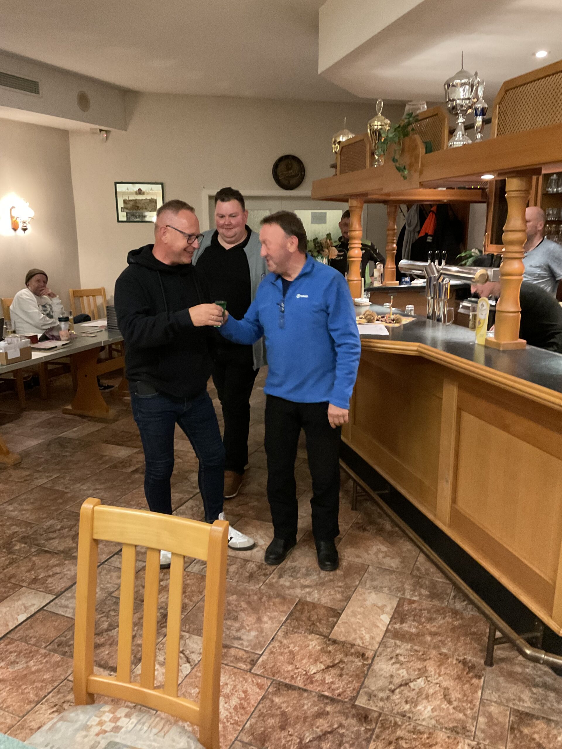 Heinz erfüllt sein Versprechen: ein grüner Lauterbacher für Michael – strahlende Gesichter am Skattisch.