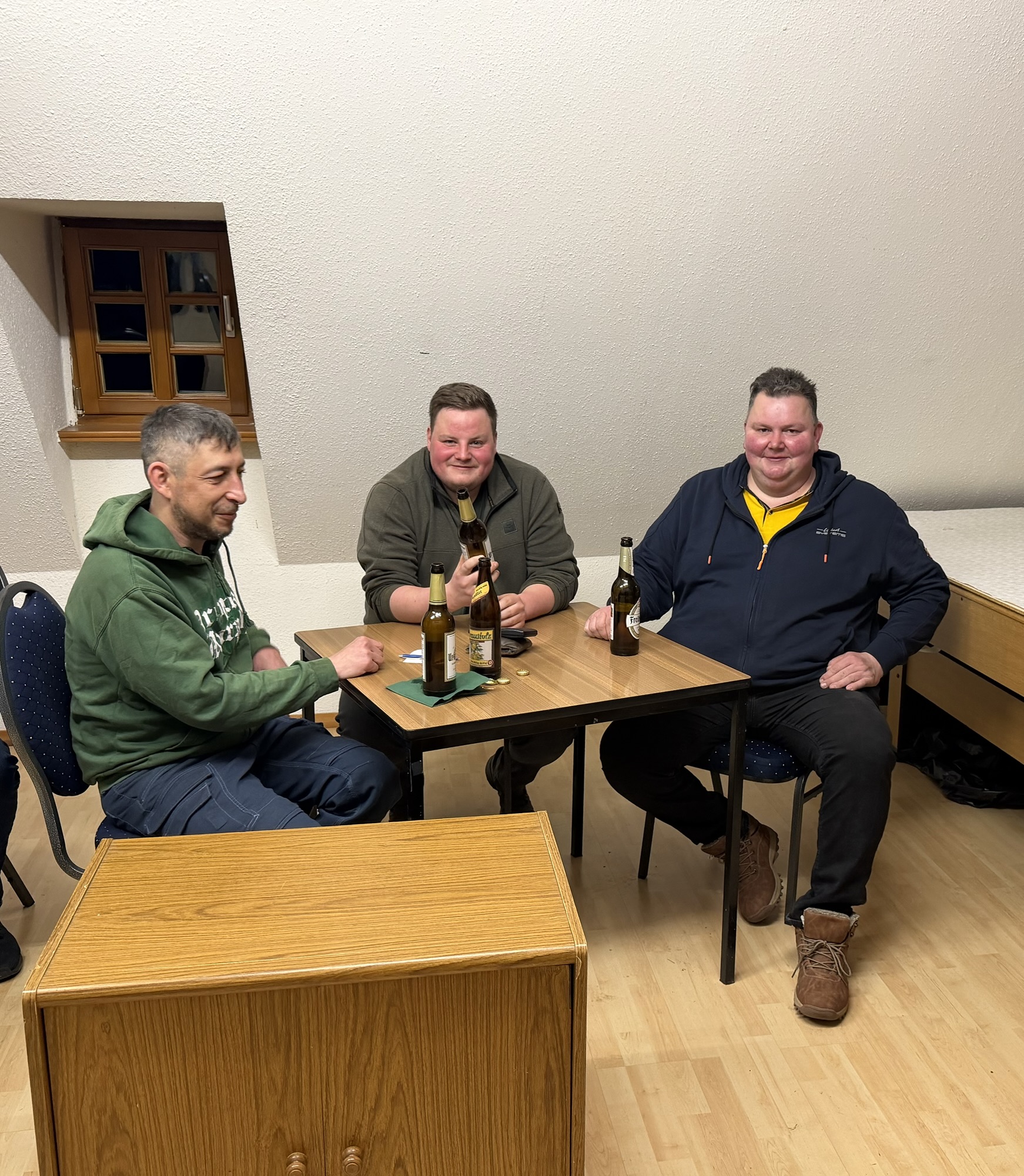 Drei Sieger sitzen am Tisch und stoßen mit Bier an.