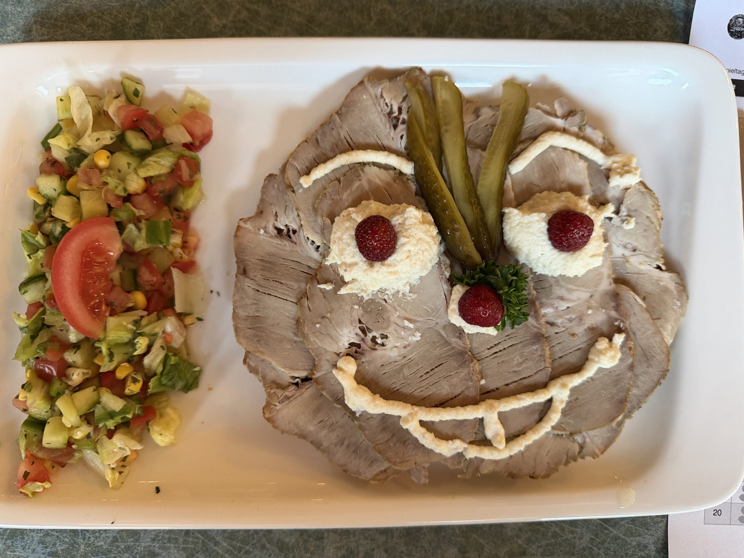 Liebevoll angerichtete scharfe Sache mit Braten, Meerrettich, Erdbeeren, Gurken und Salat als lustiges Gesicht
